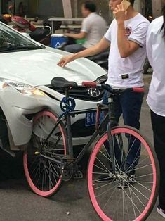 a man talking on his cell phone while standing next to a bike with a pink rim