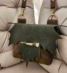 a green leaf purse sitting on the back of a couch with two handles and straps