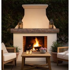 an outdoor fireplace with two chairs and a coffee table in front of it, surrounded by greenery