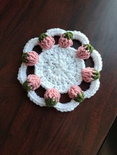 a crocheted dishcloth with pink flowers on it sitting on a wooden table