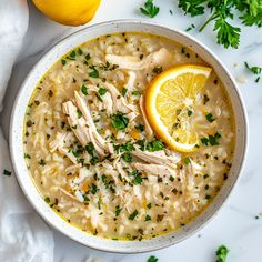 a bowl filled with chicken and rice soup next to two lemons on the side