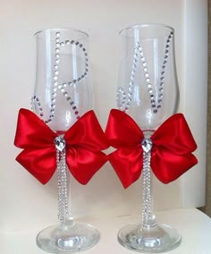 two wine glasses decorated with red bows and silver beaded monogrammed letters are sitting side by side on a white surface