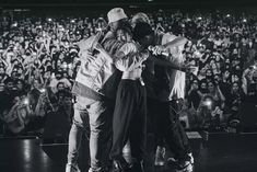 two men hugging each other in front of a large crowd at a concert with their arms around one another