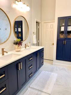 a bathroom with blue cabinets and two mirrors on the wall next to each other, along with a white rug