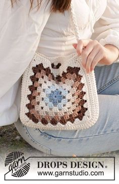 a woman sitting on the ground holding a crocheted purse