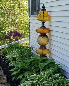 three yellow glass vases are hanging from the side of a house in front of some plants