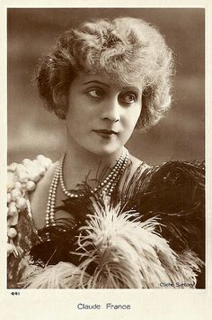 an old black and white photo of a woman with pearls on her necklace, holding a feathered fan