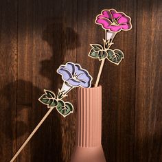 three flowers in a pink vase on a wooden table