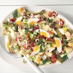 a white plate topped with salad and an egg on top of it next to a spoon