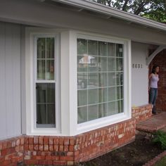 a woman standing in the doorway of a brick house with her hand on the window sill