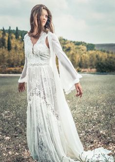 a woman in a long white dress is standing in the middle of an open field