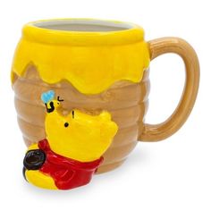 a ceramic winnie the pooh mug sitting on top of a white table next to a yellow cup