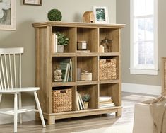 a wooden bookcase with baskets on top of it in a living room next to a white chair