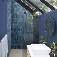 a blue tiled bathroom with two sinks and a skylight over the shower area is seen in this image