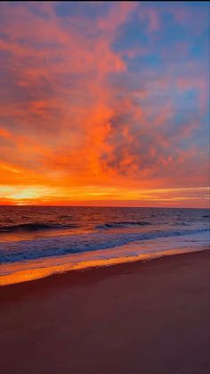 an orange and blue sunset over the ocean with waves coming in to shore on a sandy beach