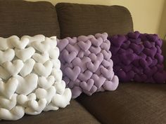 three pillows made to look like hearts are sitting on a couch, one is purple and the other is white