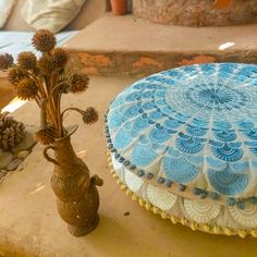 a blue and white decorative pillow sitting on top of a table next to a vase