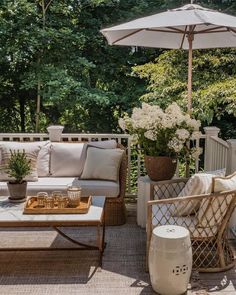 an outdoor living area with wicker furniture and white flowers on the table under an umbrella