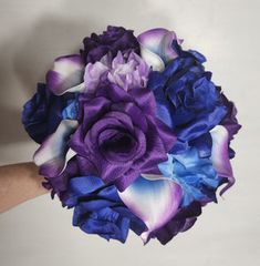 a bridal bouquet with purple and blue flowers on it is being held by someone's hand