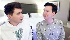 two young men sitting next to each other on a bed in a room with white sheets