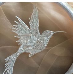 a bird made out of crystal beads on a metal bowl with white ribbon around it