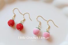 three tiny crocheted strawberrys are hanging from gold earwires on a white surface