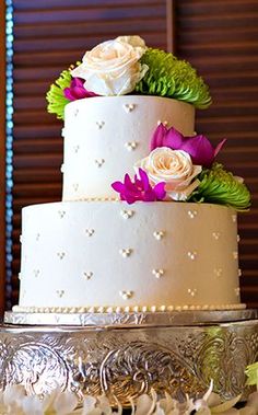 a wedding cake with white frosting and purple flowers on the top is sitting on a silver platter