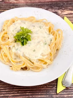 a white plate topped with pasta covered in sauce and garnished with a green leaf