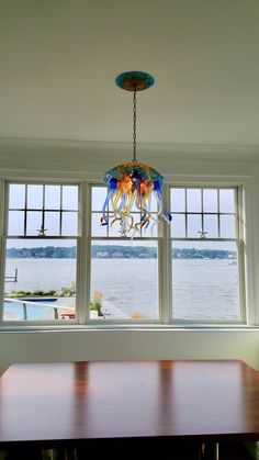 a chandelier hanging over a wooden table in front of a window overlooking the water