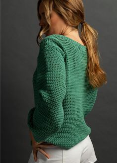 a woman in white shorts and a green sweater is looking down at her back while she has her hands on her hips