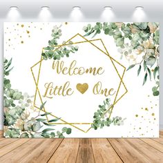 an image of a welcome little one sign with flowers and greenery on the wall