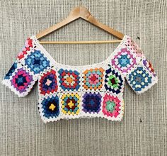 a colorful crocheted top hanging on a wooden hanger with a white background