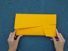 two hands holding an origami envelope against a blue wall with yellow tape on it