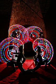 two people sitting on the ground with some lights in front of them and one person standing next to each other