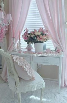 a white desk topped with a vase filled with flowers next to a pink curtained window