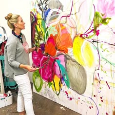 a woman standing in front of a painting on the wall with flowers painted on it