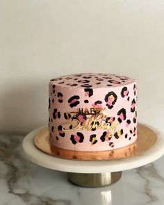 a pink leopard print cake sitting on top of a white cake plate with gold lettering