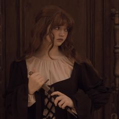 a woman with long hair holding a knife in front of a wooden door and looking at the camera