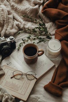 an open book with glasses and a camera on top of it next to a cup of coffee