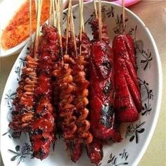 several skewers of meat on a plate with dipping sauce