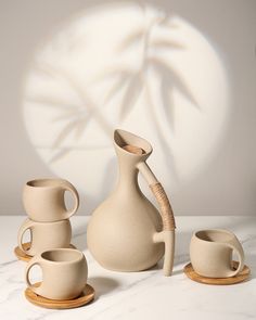 three white vases and two cups on a table