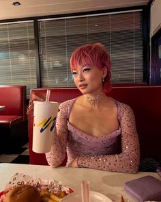 a woman with pink hair sitting at a table in front of a hamburger and drink