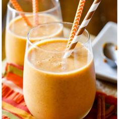 two glasses filled with orange smoothie on top of a table next to cinnamon sticks