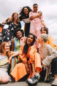 a group of women sitting next to each other on top of a cement ground with clouds in the background