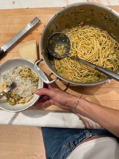 a person is holding a spoon over some pasta in a pan on a wooden table