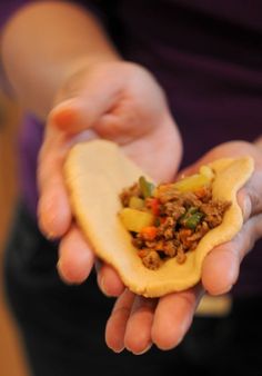 a person holding a taco in their hands with meat and veggies on it