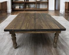 a wooden table sitting on top of a white rug in front of a book shelf