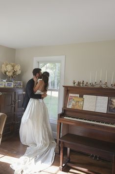 a bride and groom kissing in front of an upright piano with their arms around each other