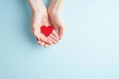 two hands holding a red heart against a blue background