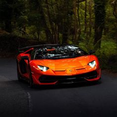 an orange sports car is driving down the road in front of some trees and bushes